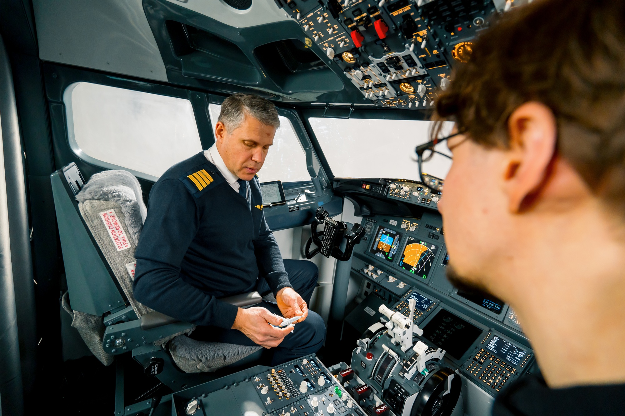 An experienced pilot instructs a young student before a training flight in the cockpit simulator